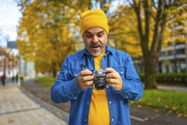 Mature man tourist checking the pictures on the screen of a camera while photographing the city during autumn