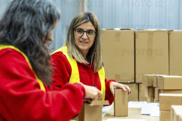 Two adult caucasian women talking relaxed while working in a distribution warehouse preparing boxes to deliver