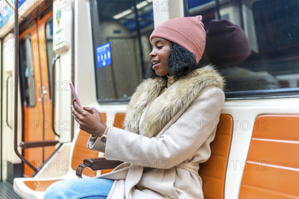 Stylish young woman commuting on a subway train, using her smartphone to browse social media and stay connected during her journey