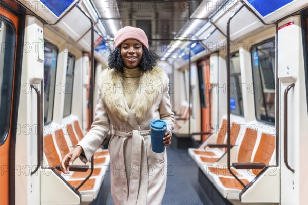 Stylish young woman walking through a subway car while holding a reusable coffee cup, enjoying her commute