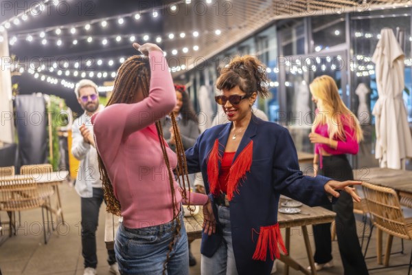 Women dancing next to multiracial friends at night party in the terrace of a bar