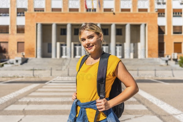 Blonde student with rucksack posing proud in the entrance of the university
