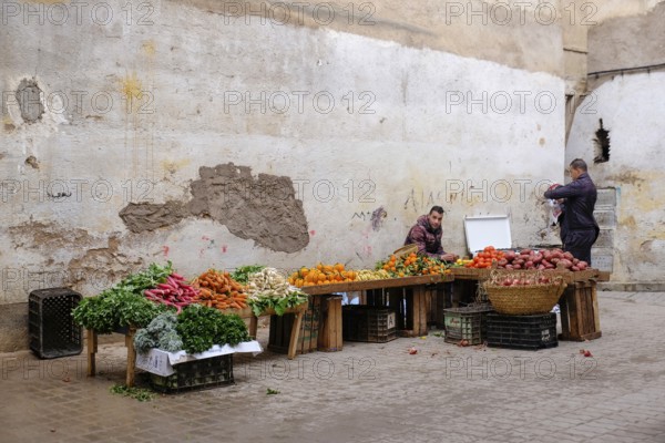 Two men selling vegetables in front of an old, plastered wall at a market, Fez, Morocco, Africa