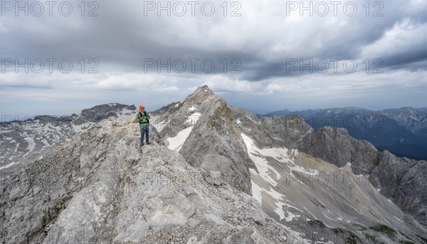 Mountaineer with helmet on a narrow rocky ridge, crossing the Jubiläumsgrat, behind the summit of the Zugspitze, Wetterstein range, Bavaria, Germany, Europe