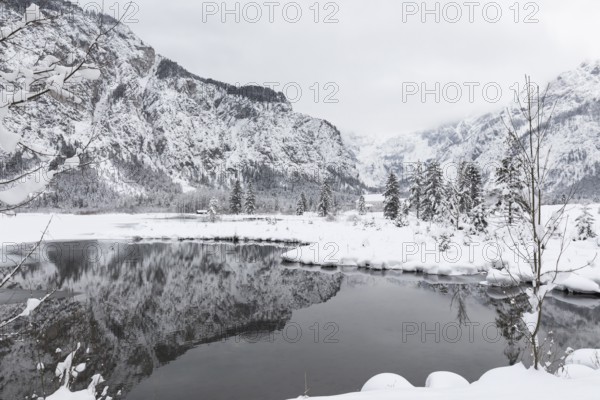 Snow covered Lake Almsee which is partly frozen and snow covered. Snow on the trees and mountains with gray overcast sky. Nearly a black and white scene