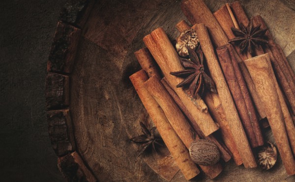 Cinnamon sticks, with nutmeg and anise star, in a wooden plate, top view, no people