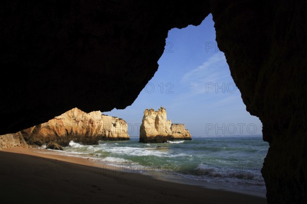 Praia do Pinhao, Lagos, Algarve, Portugal, A view from a grotto to the sea with a sandy beach and rocky formations in the background under a blue sky, Europe