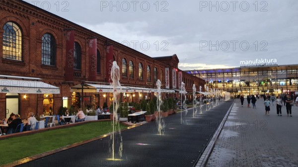 People walking along an illuminated brick façade with water features and shopping centre sign, Manufaktura, Lódz, Lodz, Lodz, Poland, Europe
