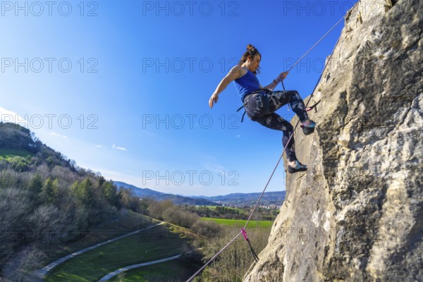 Female climber ascending a rock face, enjoying a sunny day and the beautiful view of the valley below
