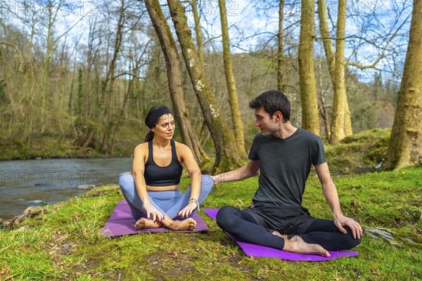 Yoga instructors performing meditation exercises by a river in a forest, enjoying the peace and quiet of nature