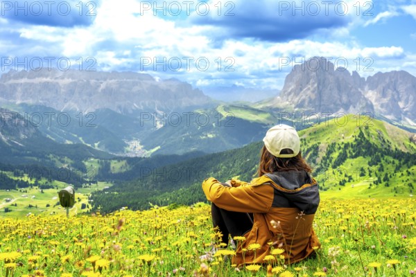 Hiker enjoying the stunning view of the seceda mountains in the dolomites during summer, surrounded by colorful wildflowers