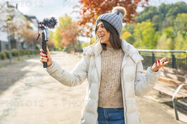 Caucasian young beauty female vlogger wearing warm winter clothes recording video in the city park