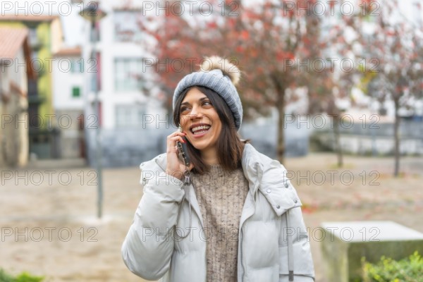 Happy and smiling caucasian young woman wearing winter clothes talking to the mobile in the city