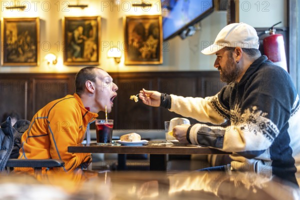 Caregiver tenderly feeds a disabled man in a restaurant, highlighting the importance of support, friendship, and inclusivity in everyday life