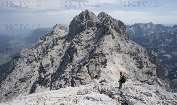 Mountaineer with helmet on a narrow rocky ridge, crossing the Jubiläumsgrat, view of rocky mountain peaks and Alpspitze, Wetterstein range, Bavaria, Germany, Europe