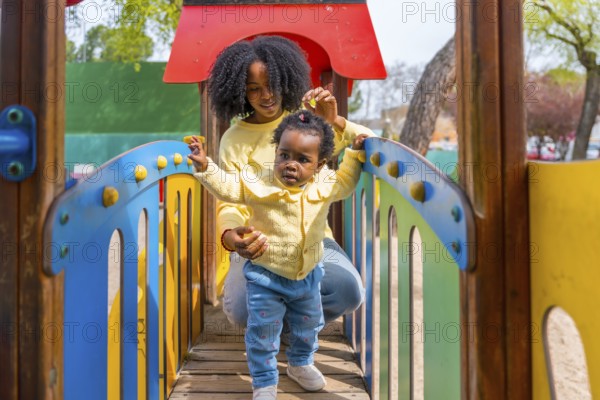 Frontal view of a young african mother and baby girl playing on playground