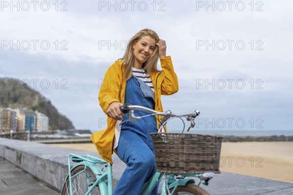 Young woman riding a bicycle along a beachfront promenade, enjoying the fresh air and coastal views