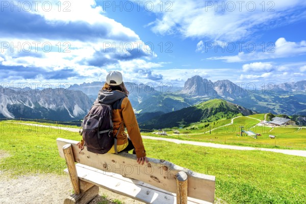 Hiker resting on a wooden bench admiring the beautiful mountain landscape of seceda in the italian dolomites on a summer day