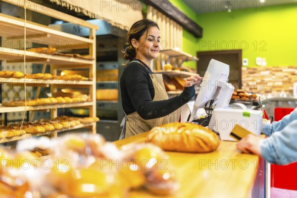 Side view photo with copy space of a latin young woman worker preparing bill for a client in an artisan bakery