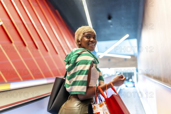 African woman using mechanical escalator in a shopping mall and turning to smile at camera