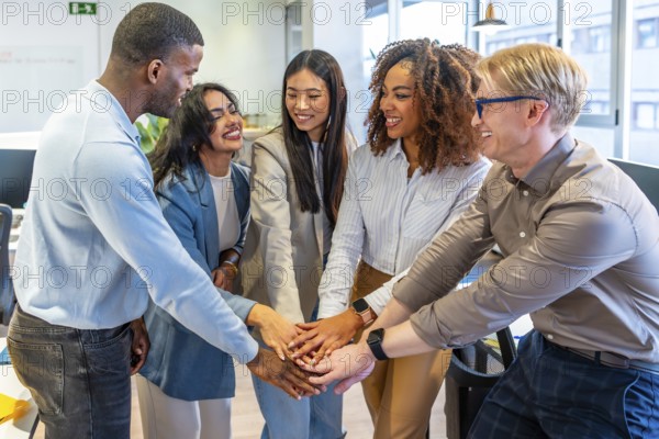 Diverse colleagues joining hands, celebrating success and teamwork in a modern coworking office