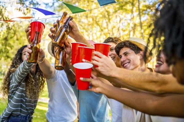 Multi-ethnic friends toasting with glasses and beer celebrating party together in a park