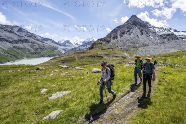 Three mountaineers on a hiking trail at a blue mountain lake, reservoir Lac des Dix, behind mountain peak Mont Blanc de Cheilon, Hérménence, Valais Alps, Valais, Switzerland, Europe