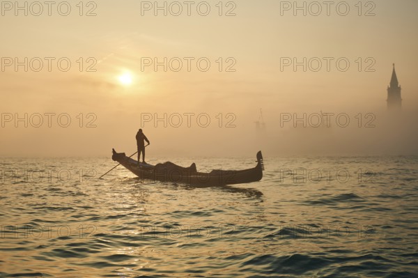 View from 'Colonna di San Marco e San Teodoro' on gondolier in front of church 'Giorgio Maggiore' on a foggy morning at sunrise in Venice in winter, Italy, Europe