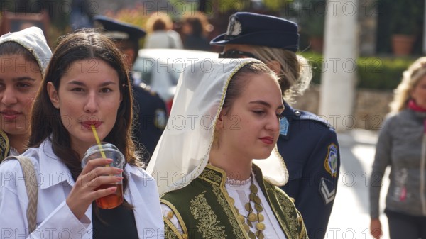 Young woman, one in traditional traditional costume, the other with a drink in her hand, on the street with police uniforms in the background, visit of Federal President Frank-Walter Steinmeier in Kandanos on 31 October 2024, Federal President, Frank-Walter Steinmeier, memorial, war crimes, Nazis, Wehrmacht crimes, World War II, Kandanos, Southwest Crete, Crete, Greek Islands, Greece, Europe