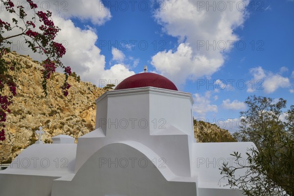 A white church with a red dome, surrounded by plants and rocks under a dramatic blue sky with clouds, Kyra Panagia, Kyra Panagia Beach, East Coast, Karpathos, Dodecanese, Greek Islands, Greece, Europe