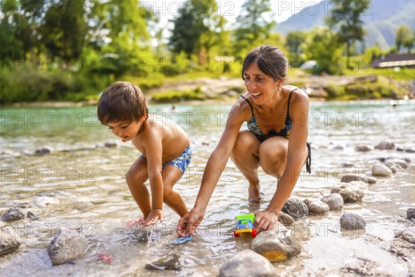Mother and son enjoying summer holidays, playing with toy cars in the refreshing water of lake bohinj, slovenia