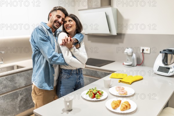 Young couple hugging in their modern kitchen, enjoying a romantic breakfast of strawberries, croissants, and donuts