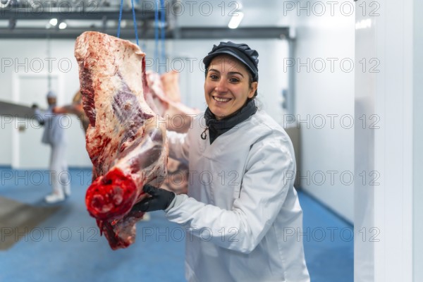 Happy female butcher carrying meat hanging in cold store of a slaughterhouse