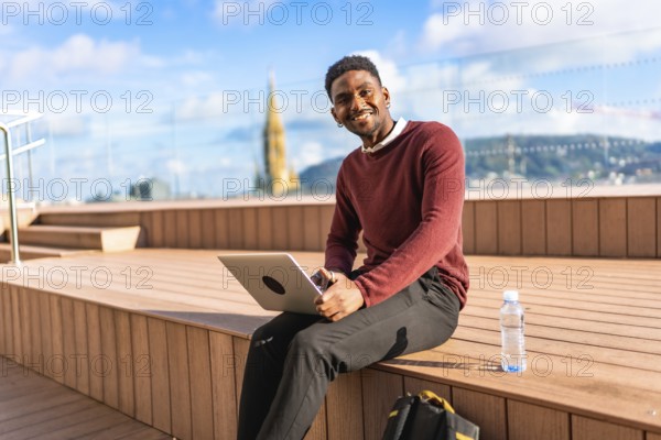 African man using laptop sitting on a terrace with views of a modern city