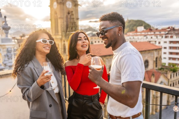 Multi-ethnic friends chatting and drinking wine in a rooftop during sunset with city views