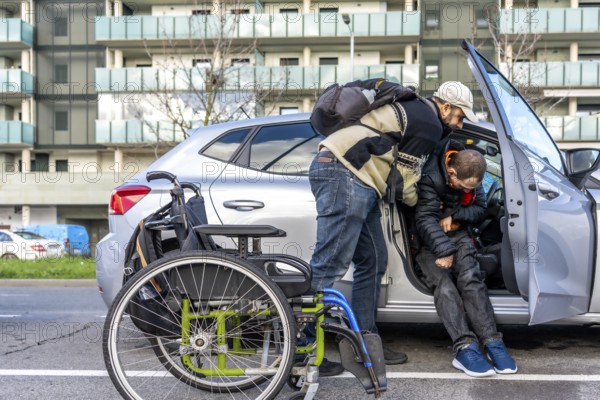 Caregiver helping young disabled man getting out of a car parked near the sidewalk in the city