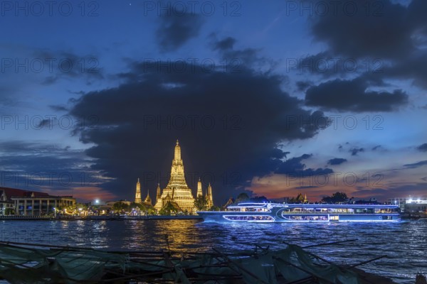 Wat Arun, Temple of Dawn at sunset with dark clouds. Boats on the Chao Phraya river. Tourist attraction in Bangkok, Thailand, Asia