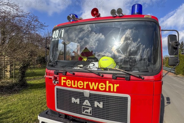 Front of red fire engine MAN truck with yellow lettering fire brigade above siren megaphone blue light, behind windscreen yellow fire brigade helmet, Germany, Europe