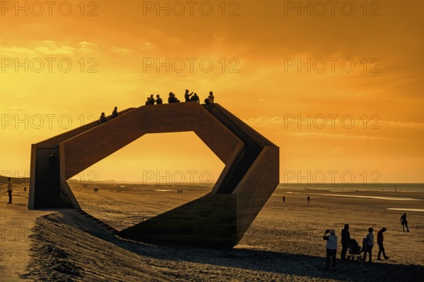 Westerpunt silhouetted against orange sunset sky, concrete sculpture on beach along North Sea coast at seaside resort De Panne, West-Flanders, Belgium, Europe
