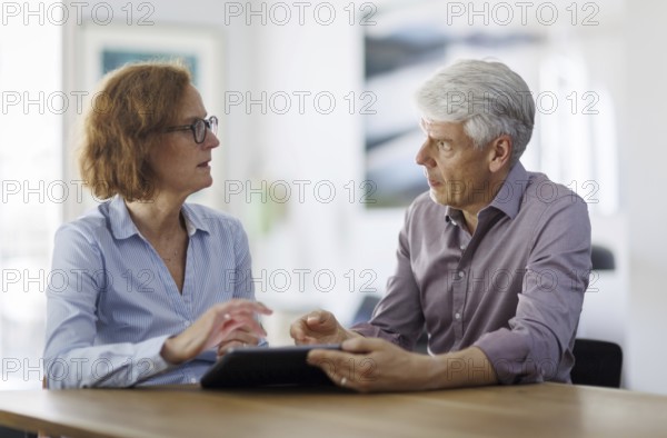 Symbolic photo. A woman and a man sit together at a table with a tablet and talk. Berlin, 13.08.2024