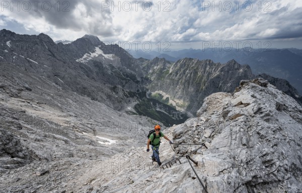 Mountaineer with helmet climbing on rock, on a narrow rocky ridge, view of Zugspitze and Höllental in steep rocky mountain landscape, crossing the Jubiläumsgrat, Wetterstein range, Bavaria, Germany, Europe