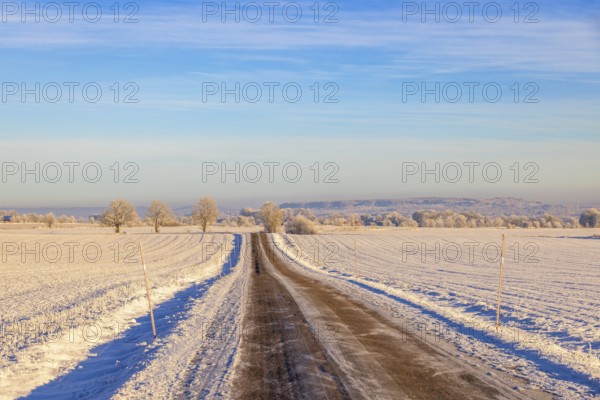 Long straight slippery country road by snowy fields in a wintry rural landscape view to the horizon, Sweden, Europe