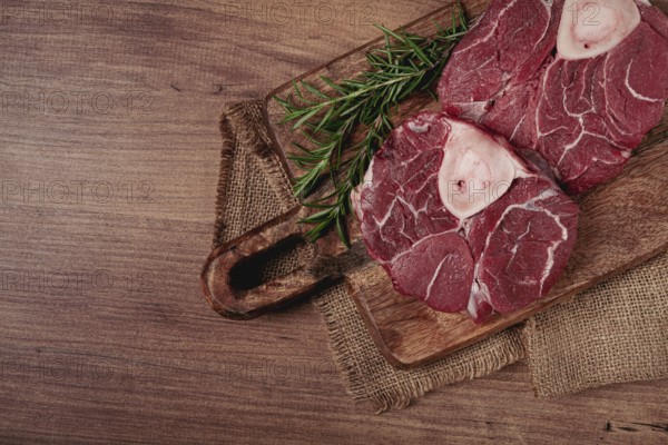 Knuckle on the bone, raw meat for ossobuco, on a wooden chopping board, with a sprig of rosemary, and spices, top view, no people