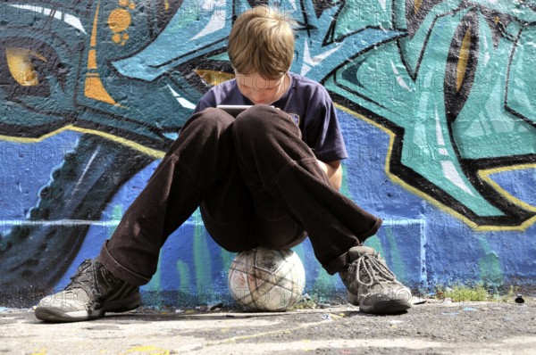 Ten-year-old boy playing with his Nintendo in front of a graffiti wall, football pitch, Germany, Europe