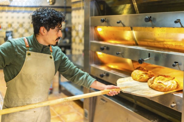 Latin young man baking bread in a traditional oven using a wooden peel