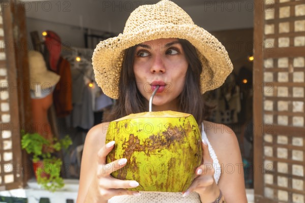 Young woman wearing straw hat enjoying refreshing coconut water during tropical vacation in siargao island, philippines
