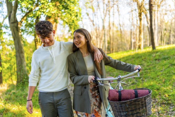 Smiling young couple walking in a sunlit park, sharing a moment together. Woman pushing a bicycle with a basket, surrounded by lush greenery