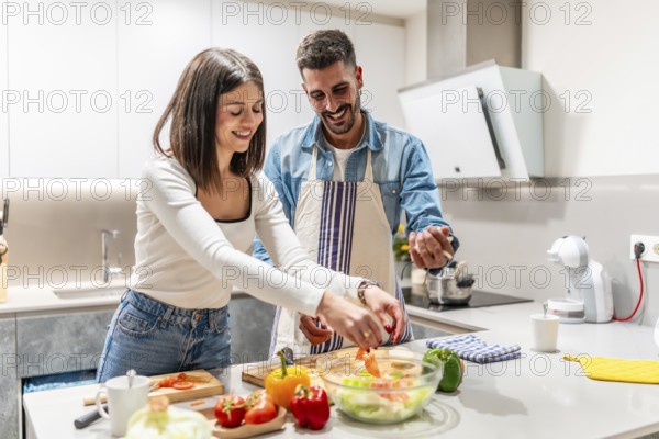 Young couple smiling and preparing a vibrant, healthy salad together in their modern kitchen, enjoying quality time and nurturing their relationship