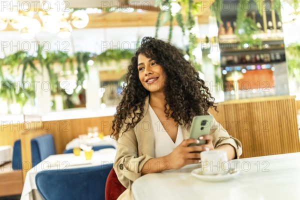 Distracted beauty latin woman using mobile while drinking coffee at cafeteria