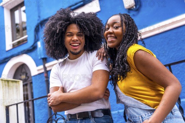 Happy african stylish couple smiling at camera leaning on a rail in a colorful street
